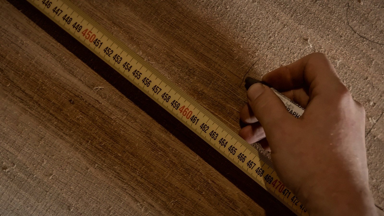 A worker marks an oak board beside a measuring tape